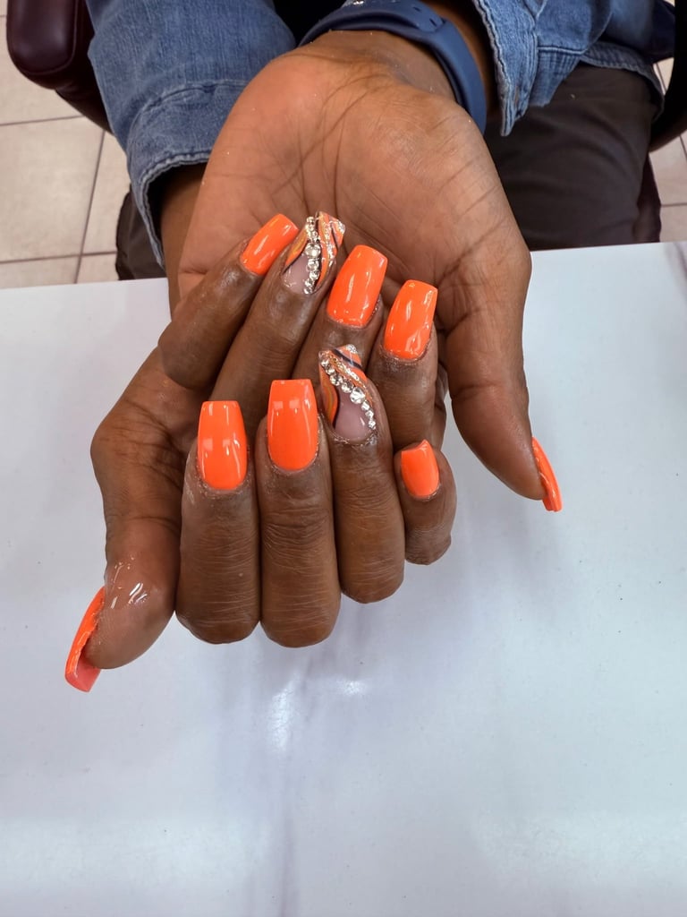 Close-up of hands with bright orange gel manicure nails featuring rhinestone accents on ring and middle fingers