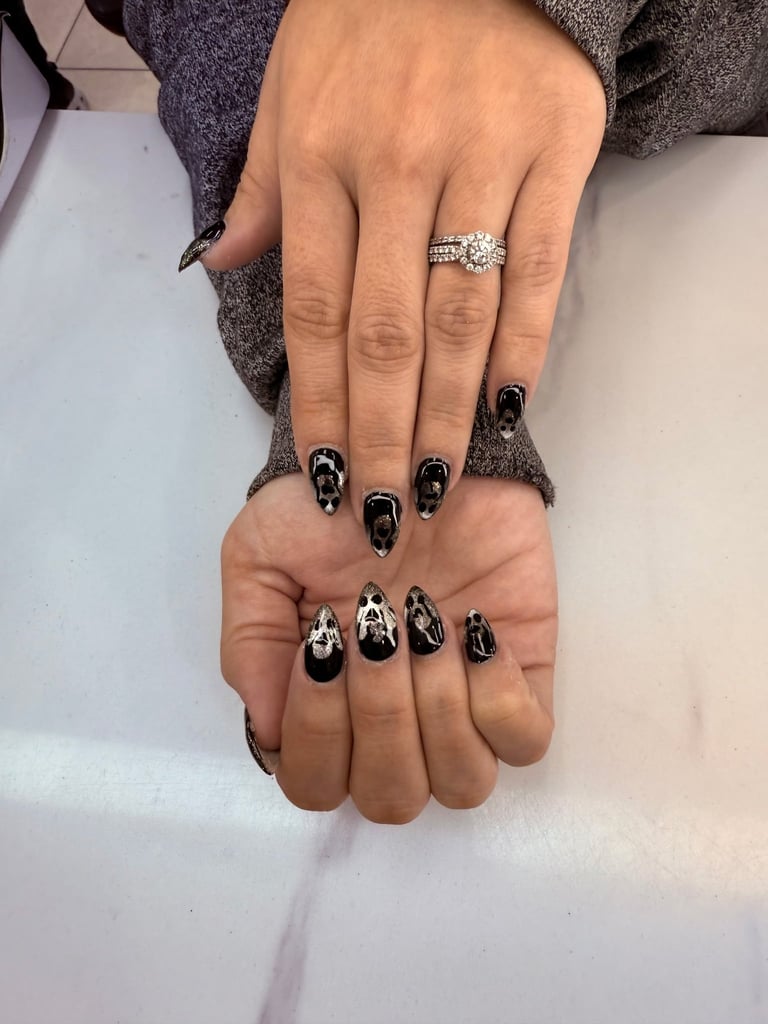 Two hands with black and white skull nail art design, one wearing a diamond engagement ring, displayed together on white surface