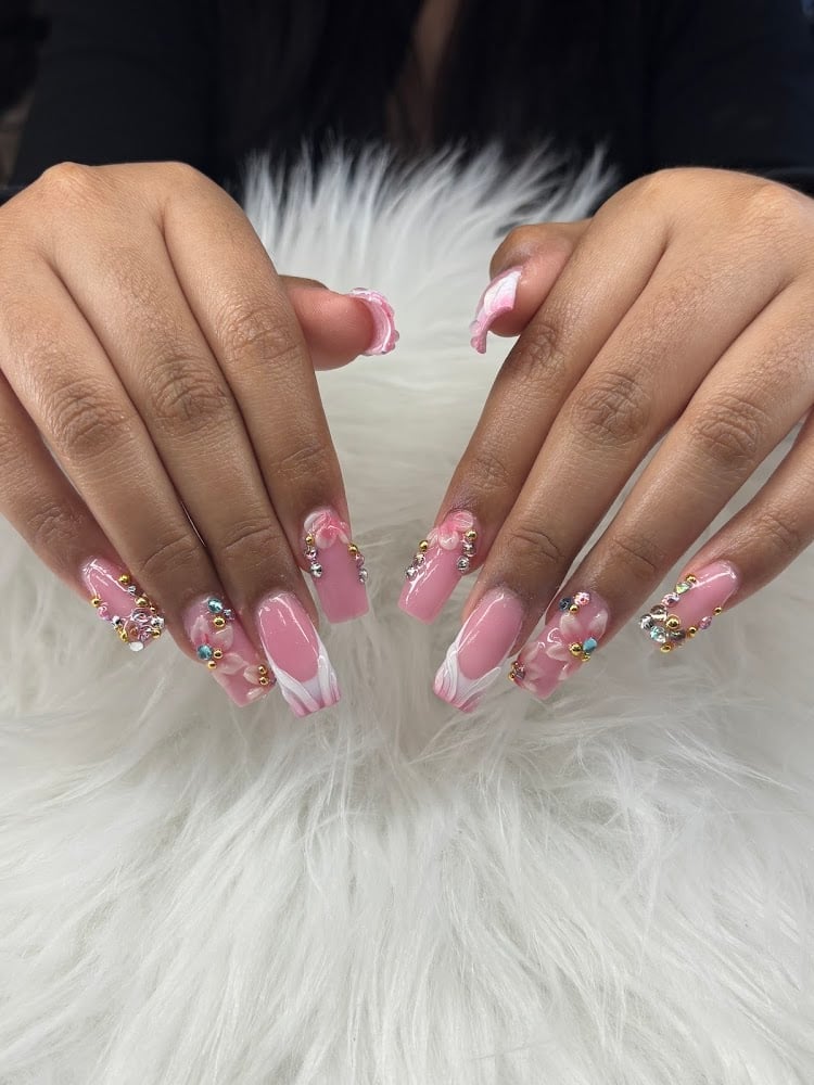 Close-up of manicured nails with pink ombre polish, rhinestone accents, and chrome details on white fluffy background