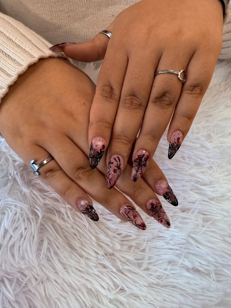 Close-up of two hands displaying stiletto nails with nude and black ombre design, wearing silver rings on white fluffy texture