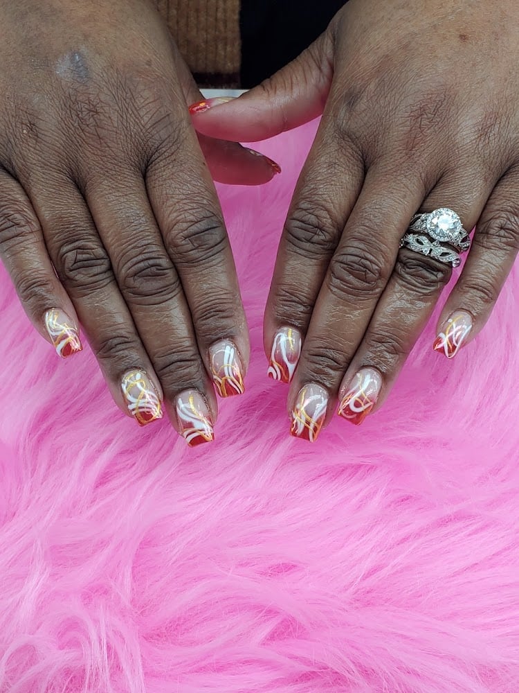 Hands with long acrylic nails featuring chrome gold and red nail art design on pink fuzzy background