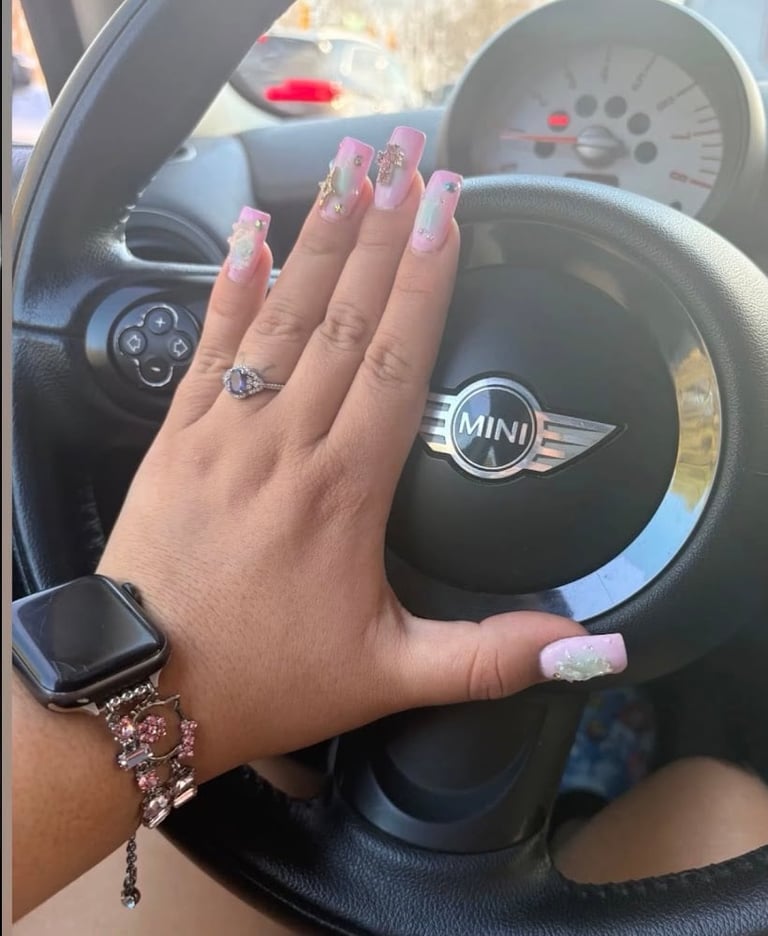 Hand with pink and white ombre nails and diamond ring on steering wheel of MINI car