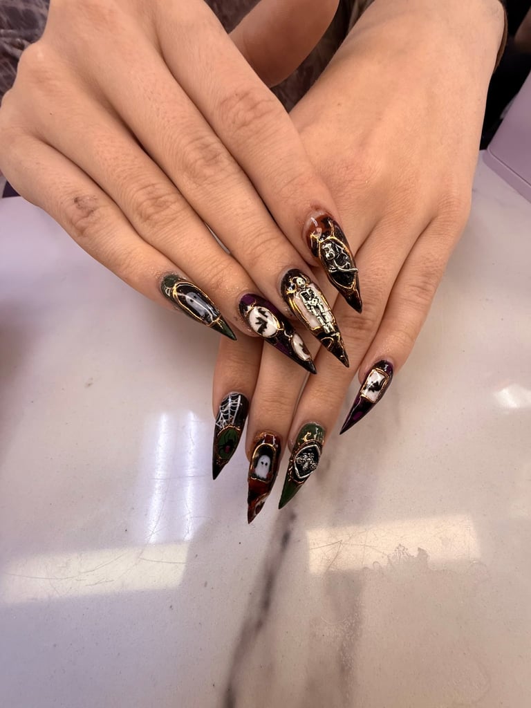 Close-up of hands displaying long stiletto nails with black, gold, and white decorative designs and metallic accents