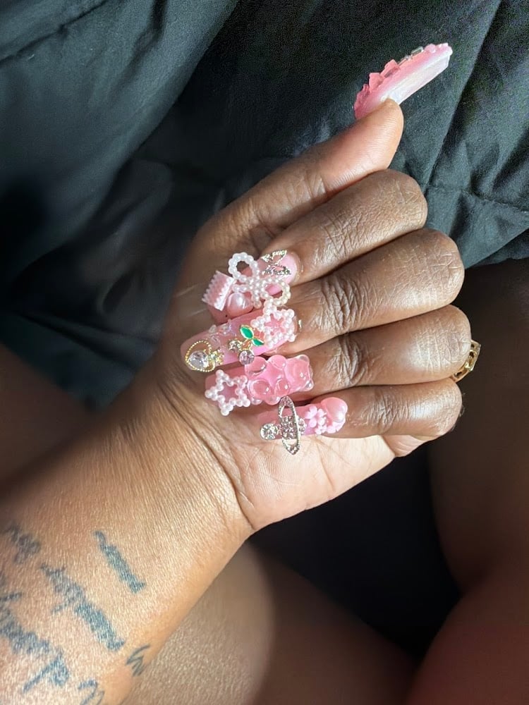Close-up of a hand displaying elaborate pink acrylic nails with rhinestone and floral embellishments