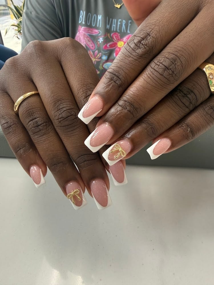 Close-up of manicured nails with white tips and pink ombre base, featuring gold geometric accents and designs