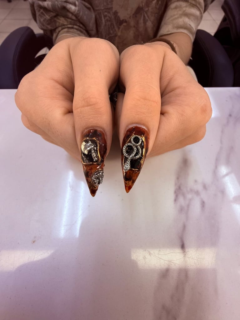 Close-up of hands displaying long almond-shaped nails with brown and gold tortoiseshell nail art design