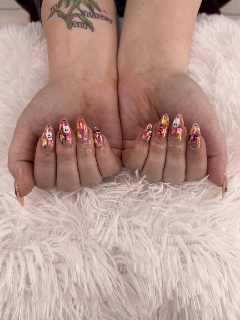 Close-up of manicured nails with red and gold foil nail art design on white fluffy surface
