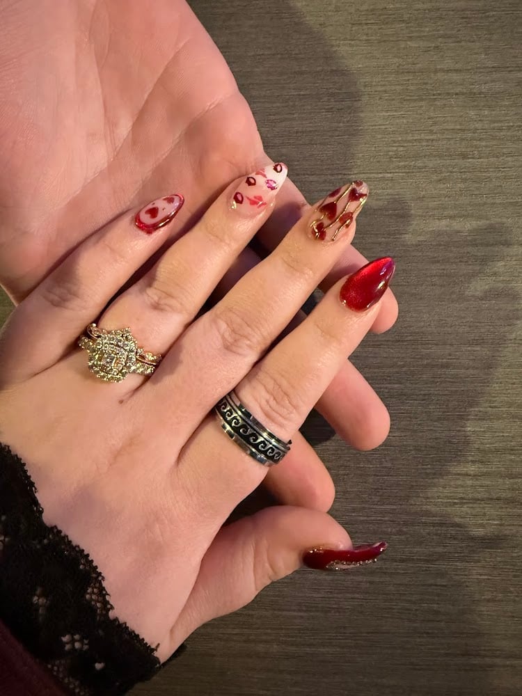 Hand displaying manicured nails with red and glitter designs, wearing decorative gold and silver rings